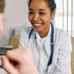 A smiling doctor in a white coat with a stethoscope provides a warm consultation.