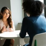 Two women sitting at a table having a professional discussion in a bright office setting.